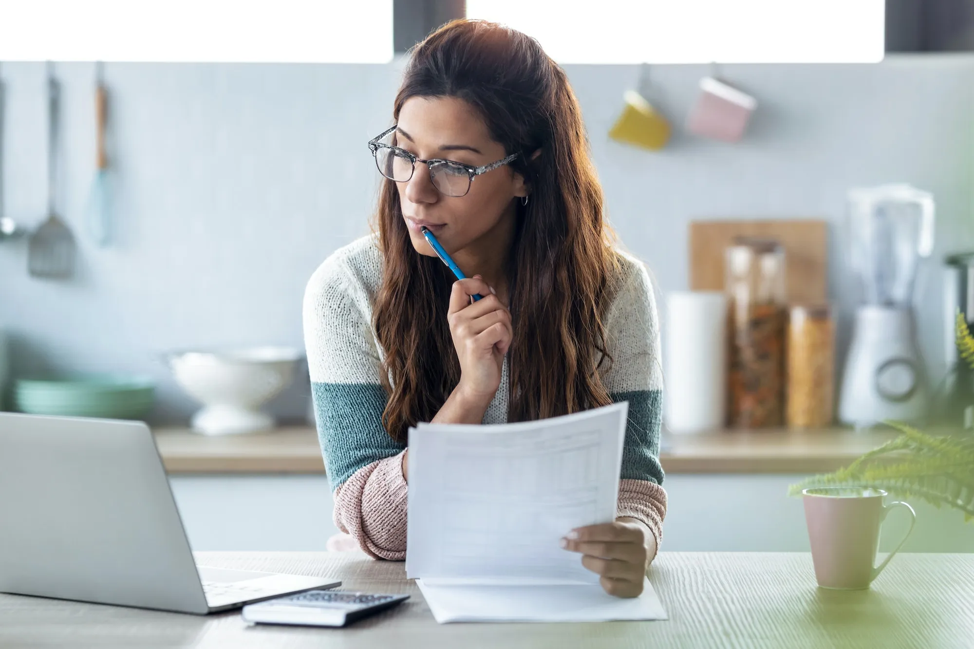 Pretty young woman working with computer while consulting some invoices and documentsat home.