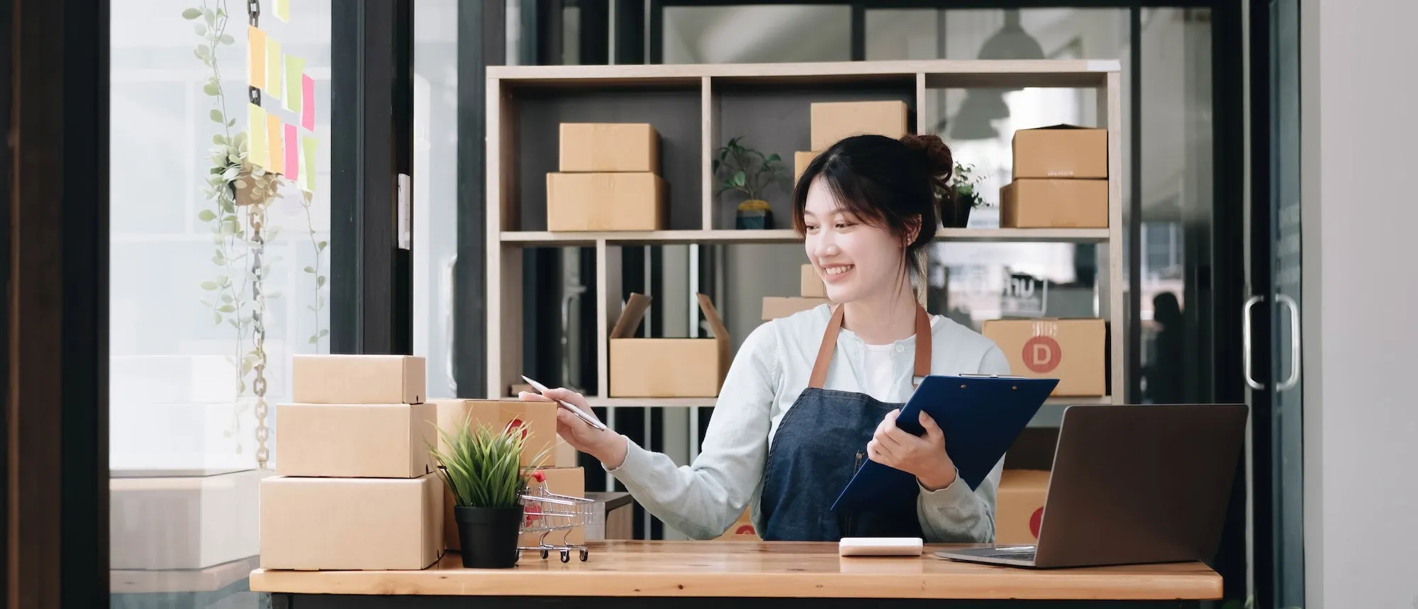 A portrait of a young Asian woman, e-commerce employee sitting in the office full of packages in the